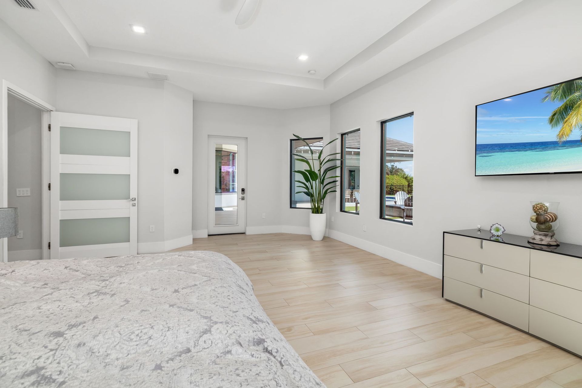 Bright modern bedroom with white walls, light wood floors, and a large bed beside ocean-view windows.