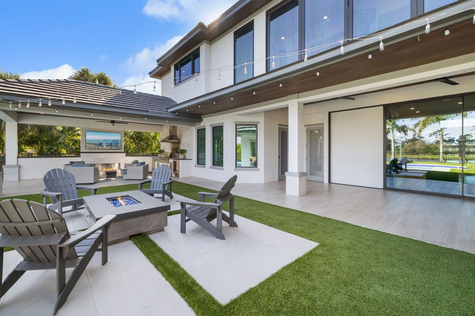 Modern patio with outdoor seating, pergola, lawn, and open sliding doors beside a house