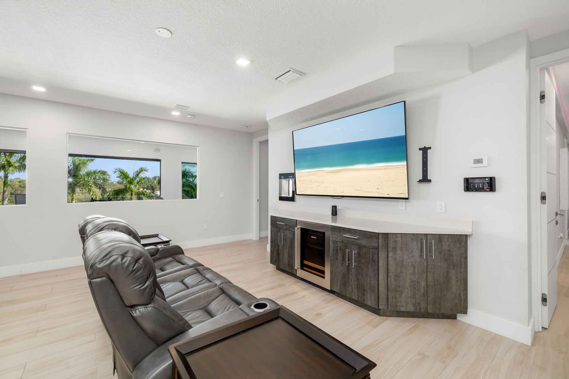 Modern living room with leather recliners, wall-mounted TV, and built-in console, bright beach view on screen