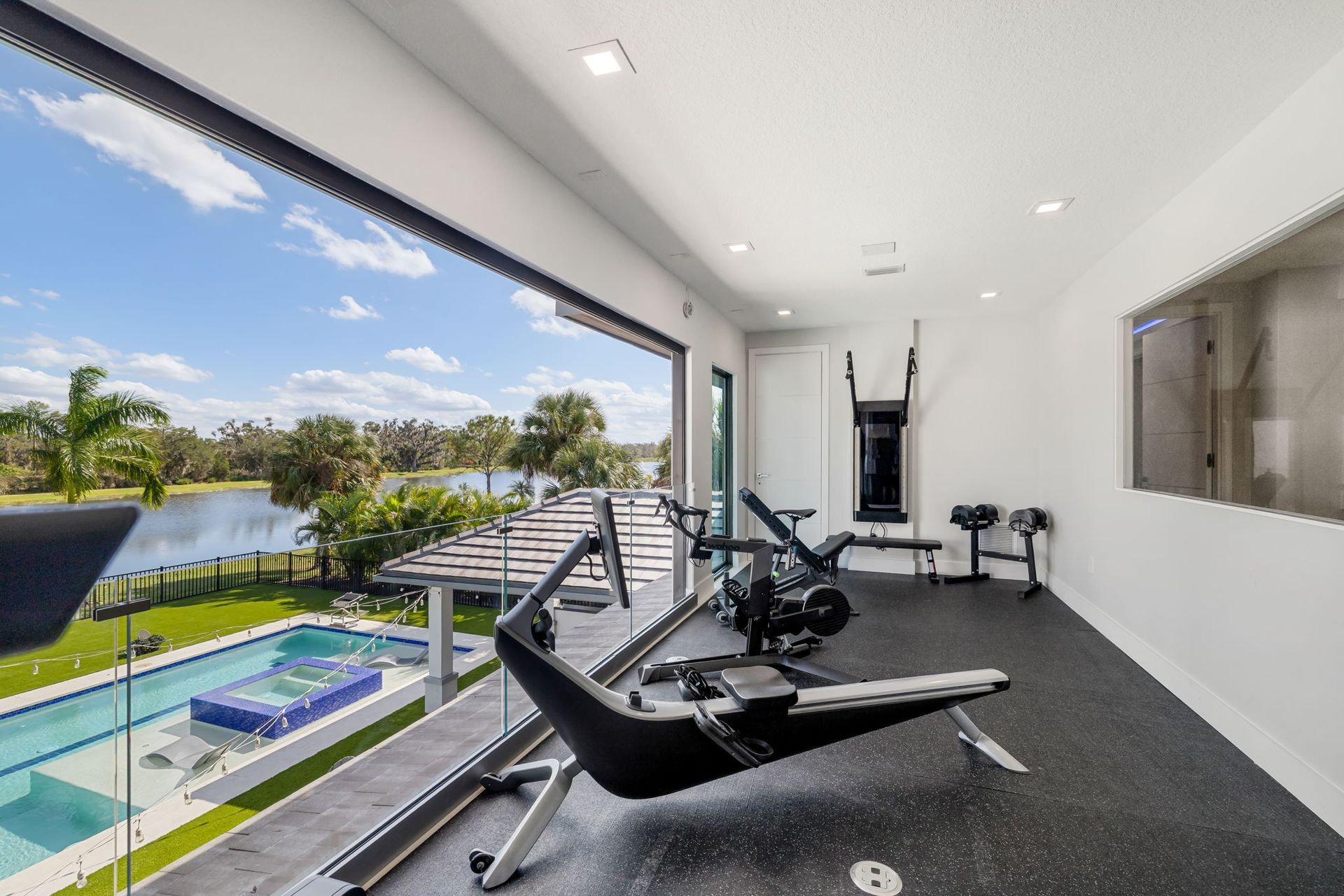 Modern gym with black equipment and floor-to-ceiling windows overlooking a pool and tropical view