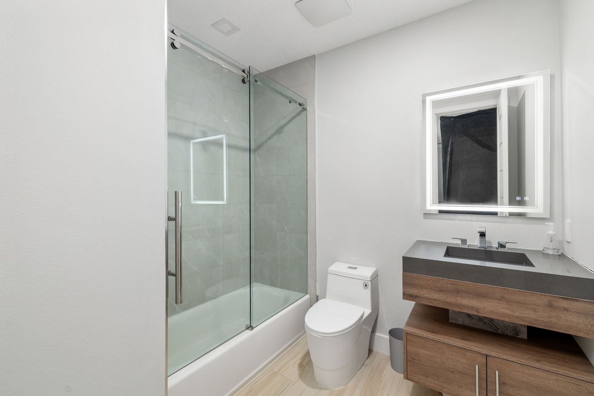 Modern bathroom with glass shower, toilet, and wood vanity with mirror.