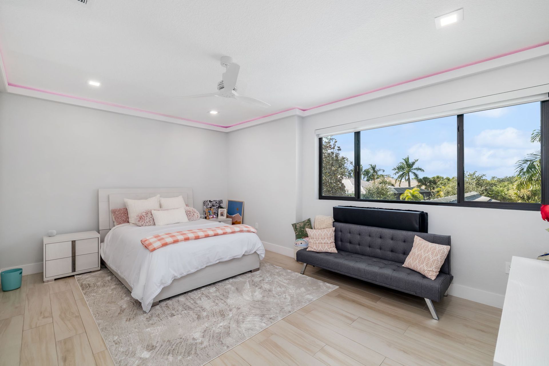 Bright bedroom with a bed, chaise lounge, and large window overlooking trees and ocean