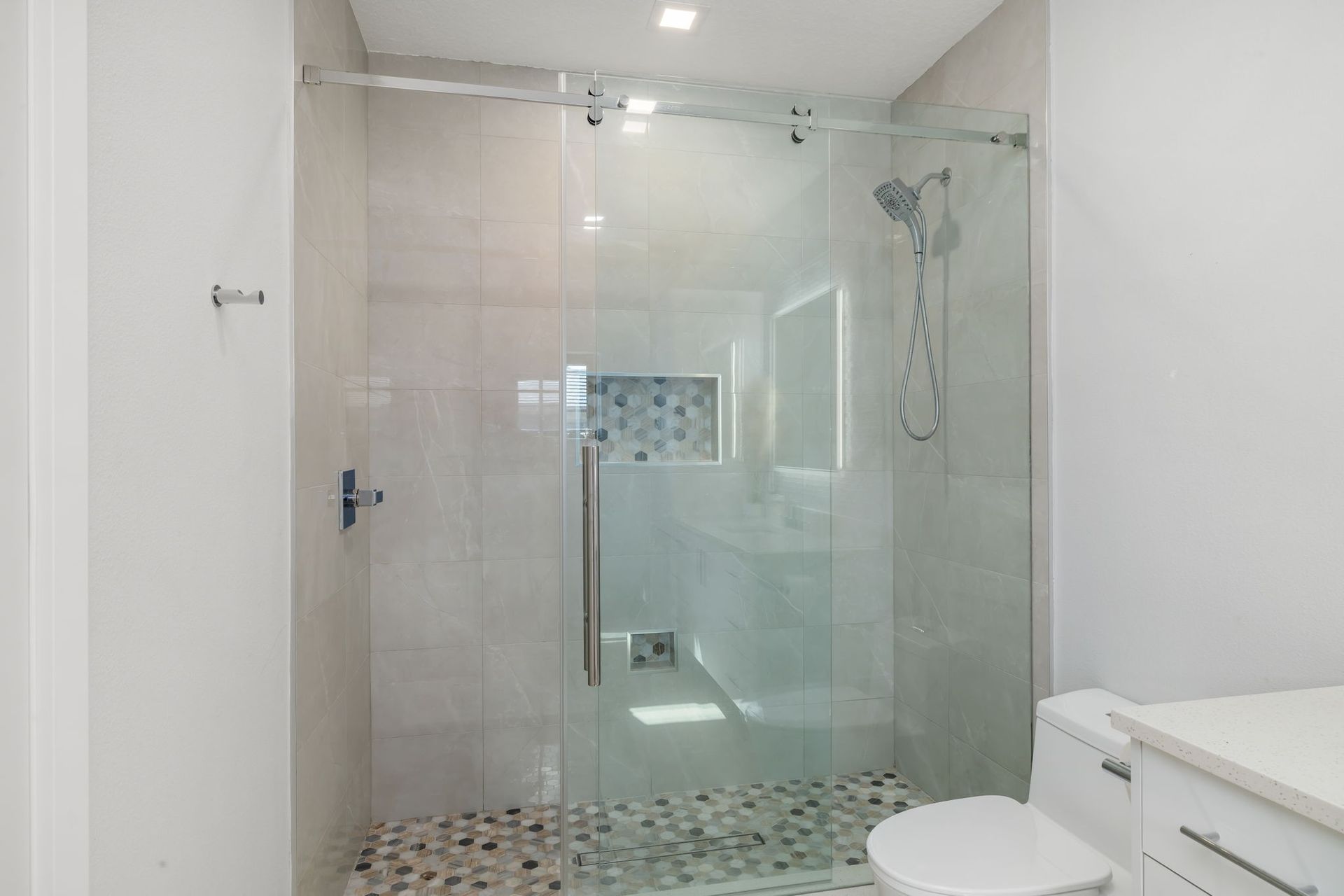 Modern bathroom with glass shower enclosure, tiled walls, pebble floor, and a toilet in the foreground