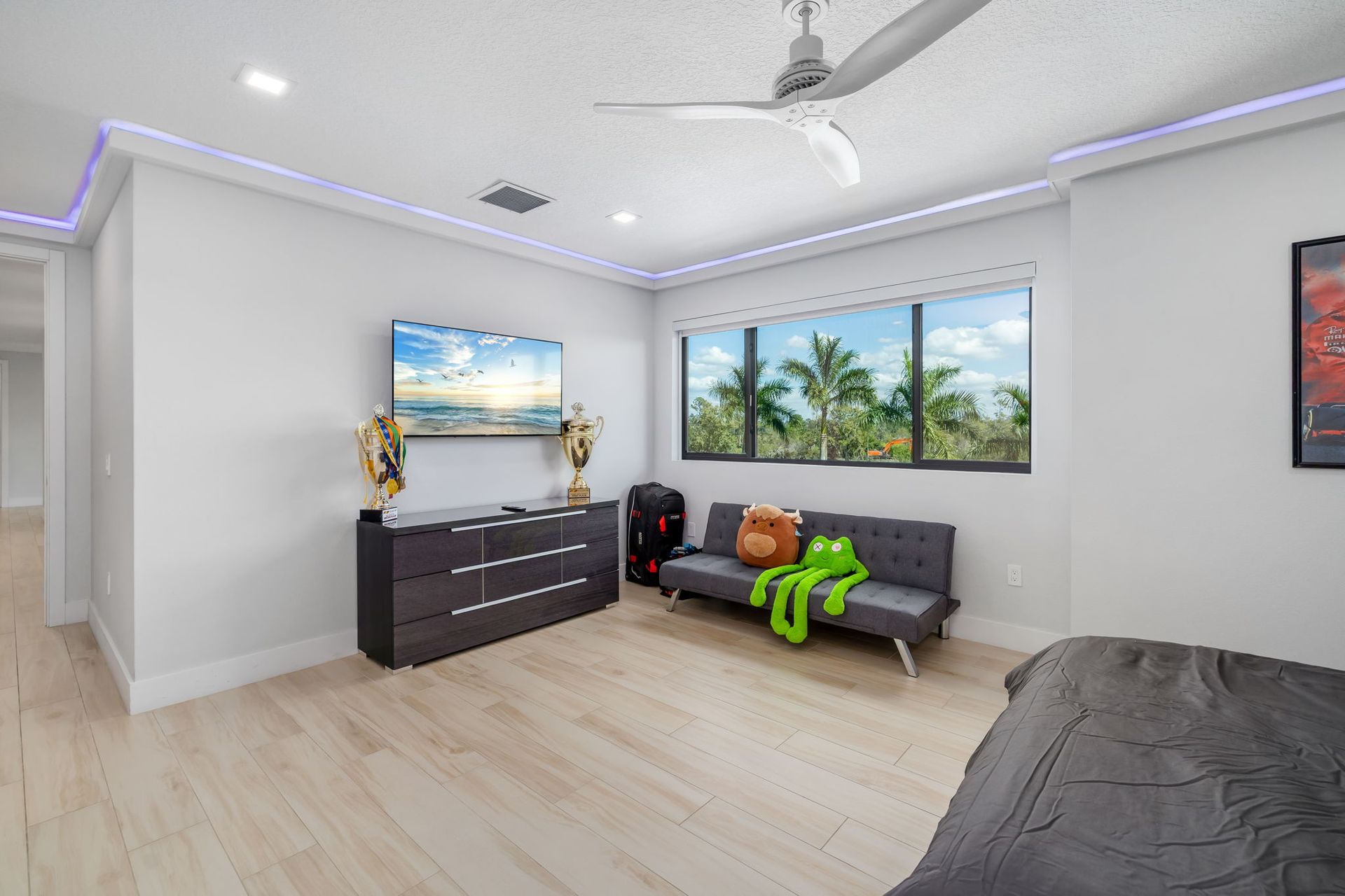 Bright bedroom with gray bed, dresser, sofa, tropical wall art, and purple LED ceiling lights