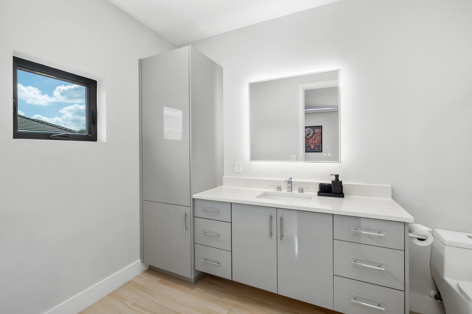 Modern bathroom with white vanity, large mirror, tall cabinet, and small wall window