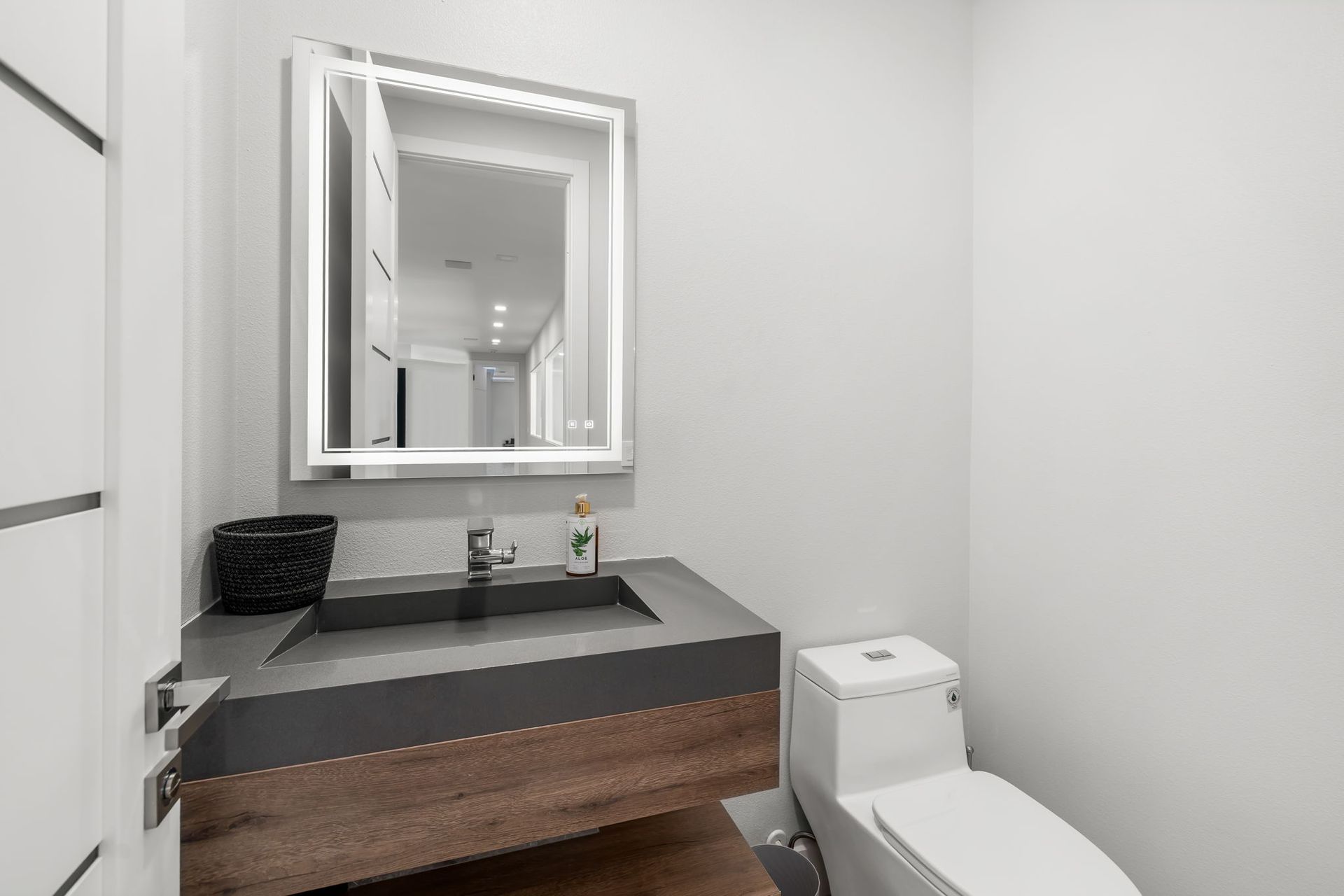 Modern bathroom vanity with dark countertop, mirror, sink, and toilet in a bright white room