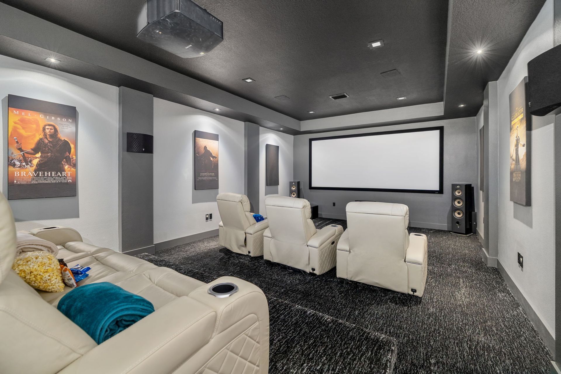 Home theater with cream reclining seats, a large projector screen, and movie posters on gray walls