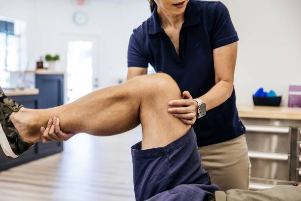 A physical therapist examines a patient's knee in an office.