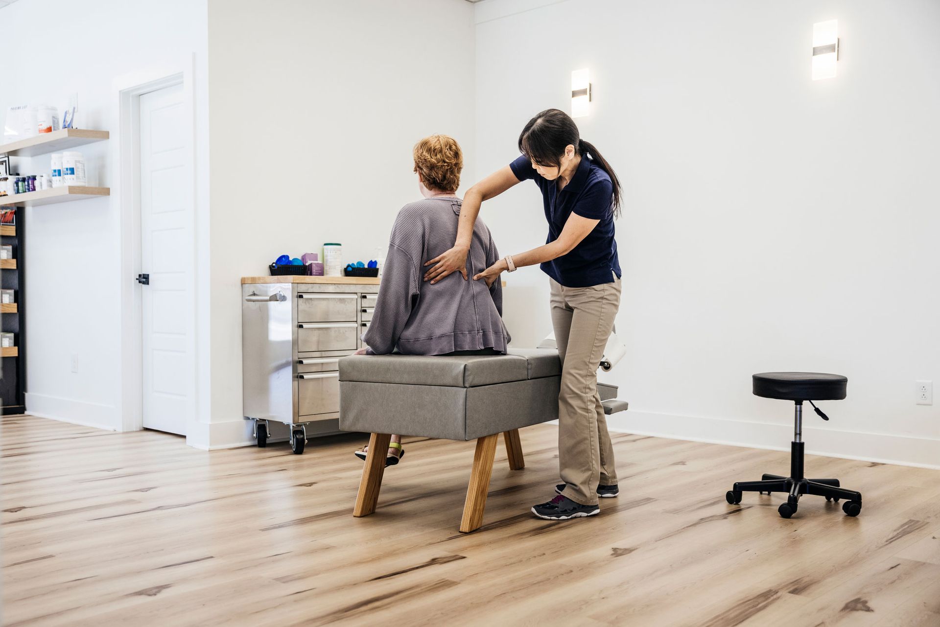 Chiropractor examining a patient's back in a light-filled office.
