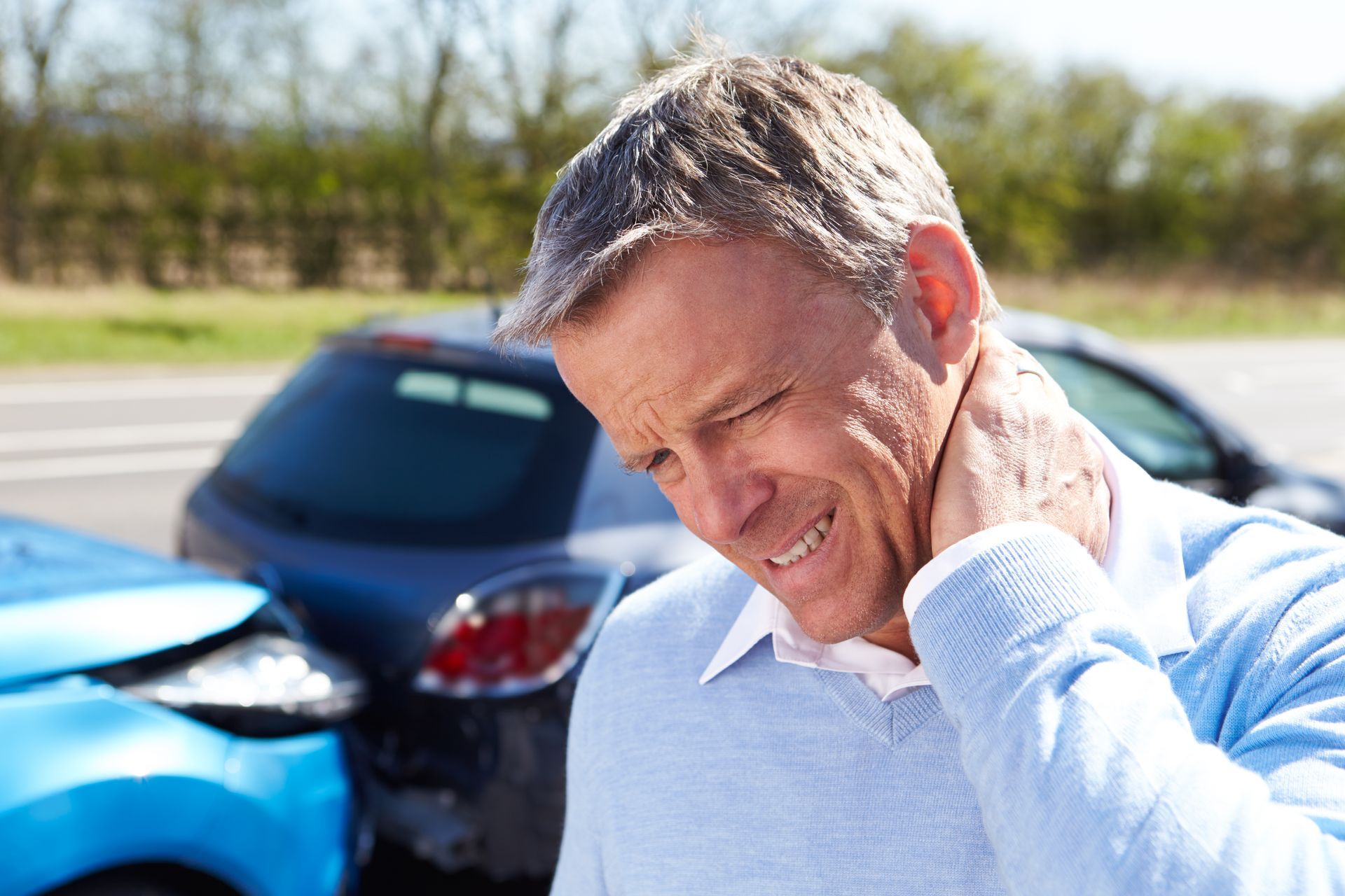 Man clutching neck, in front of damaged cars, appearing to be in pain after a car accident.