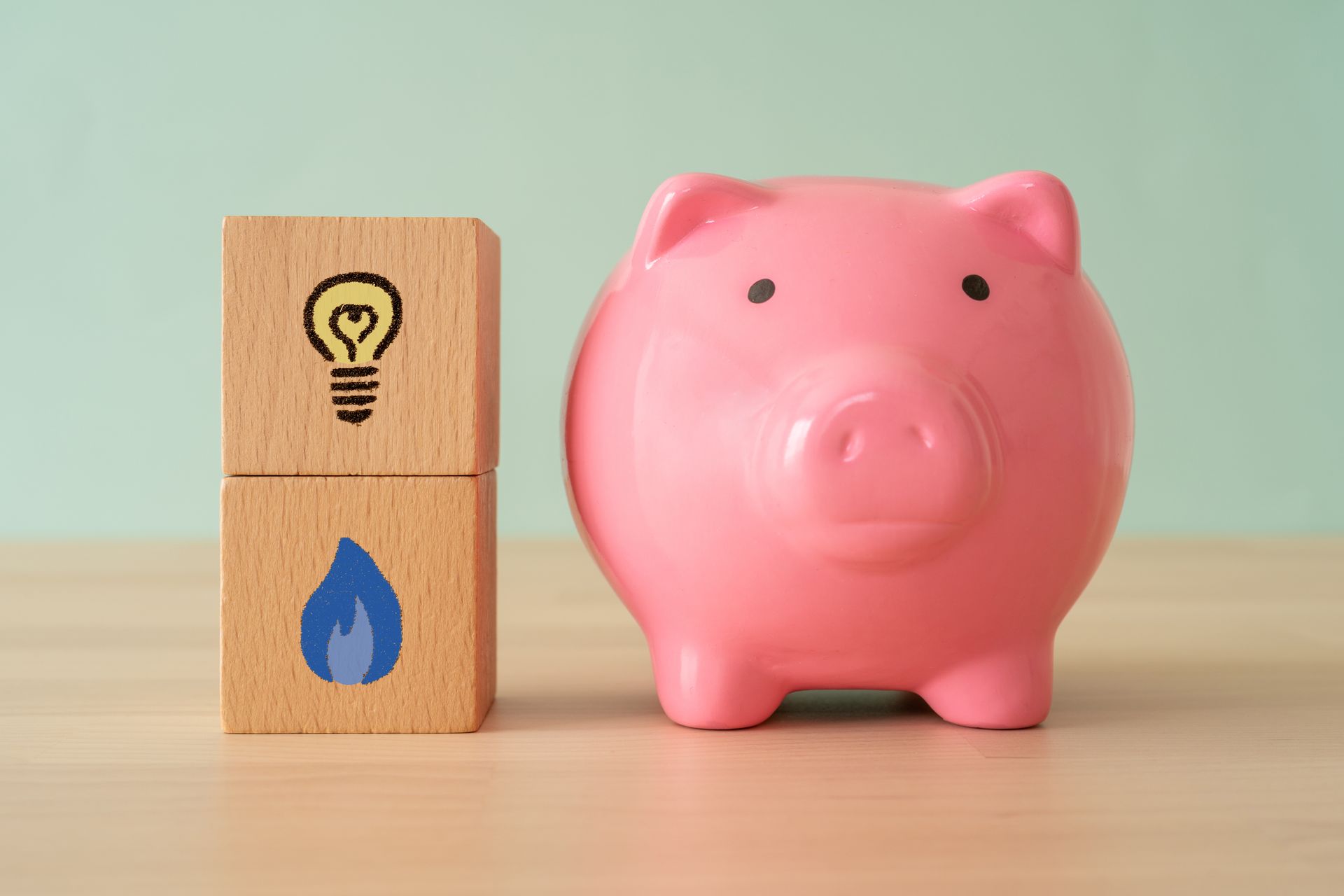 A pink piggy bank next to two blocks. One block has a light bulb and the other has a water drop.