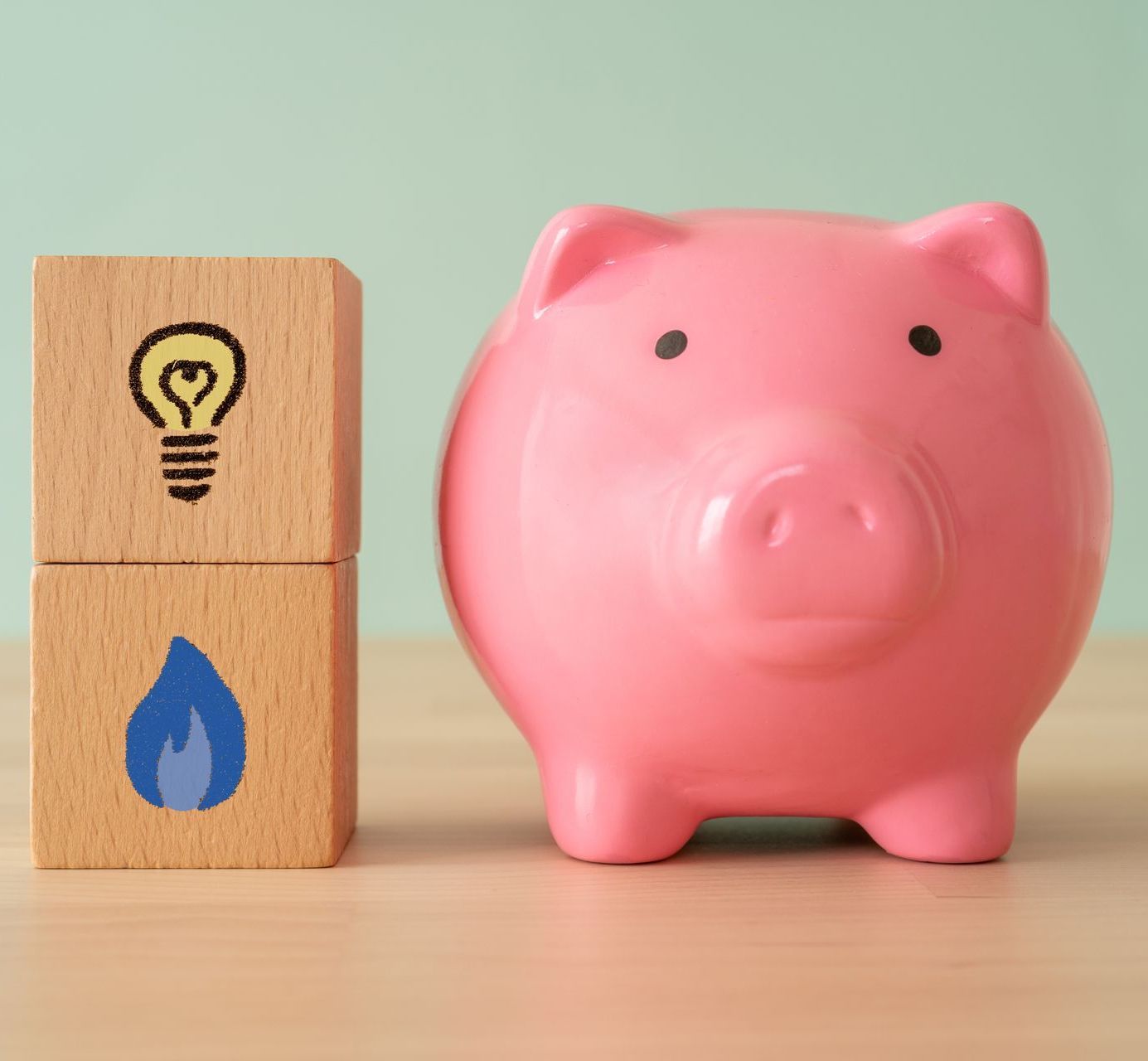 A pink piggy bank sits next to a wooden block with a light bulb and a blue flame on it