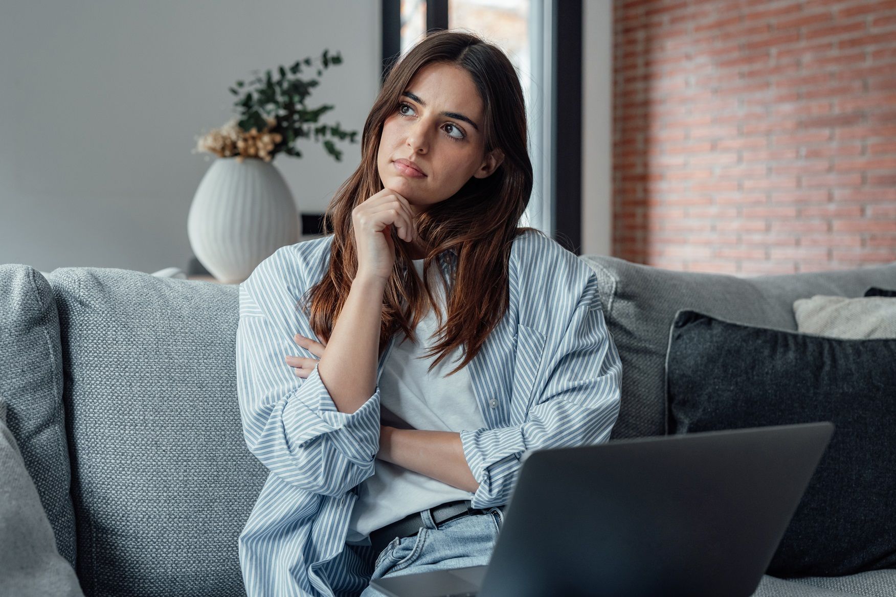 Small Steps to Ease Financial Worries and Regain Control with Miss Money Savvy A woman is sitting on a couch using a laptop computer. She looks worried about her finances.