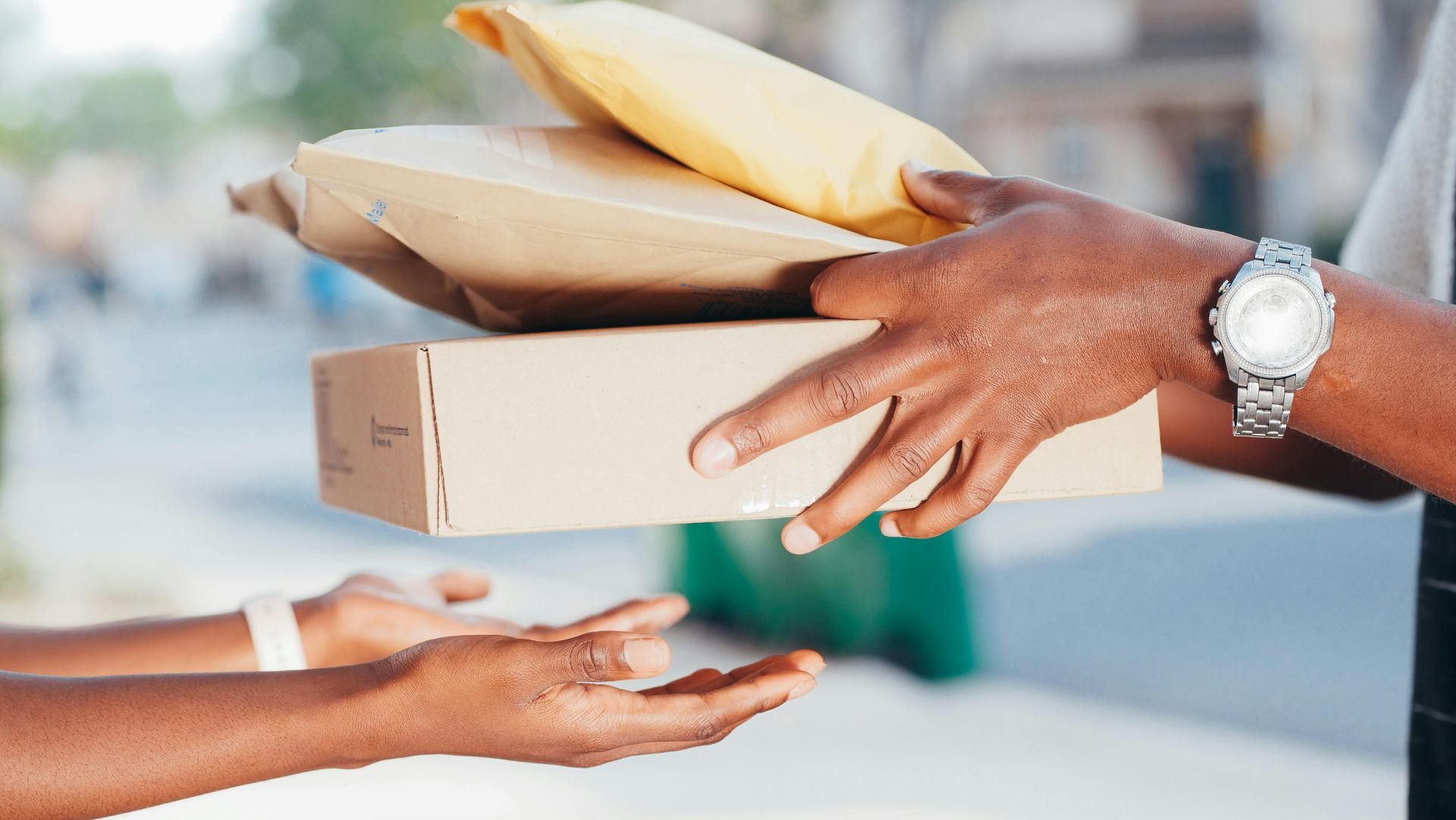 A person is handing a box and envelopes to another person. The person has received an online shopping order.