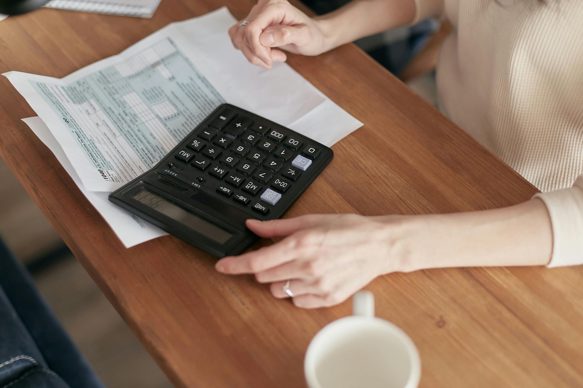 A woman is sitting at a table using a calculator trying to ease her financial worries and regain control.