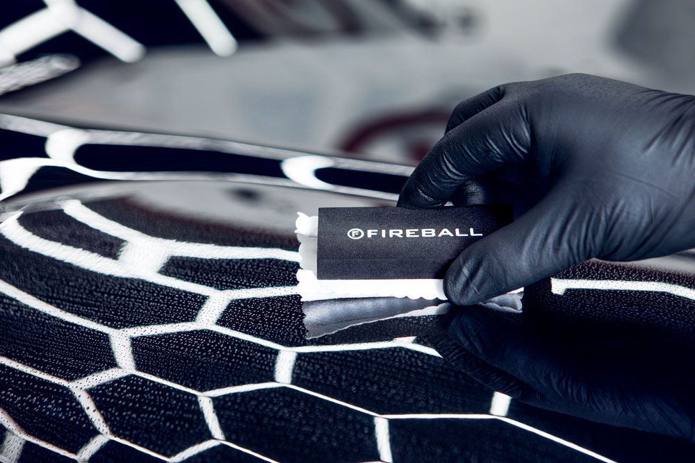 a person wearing black gloves is applying a coating to a car .