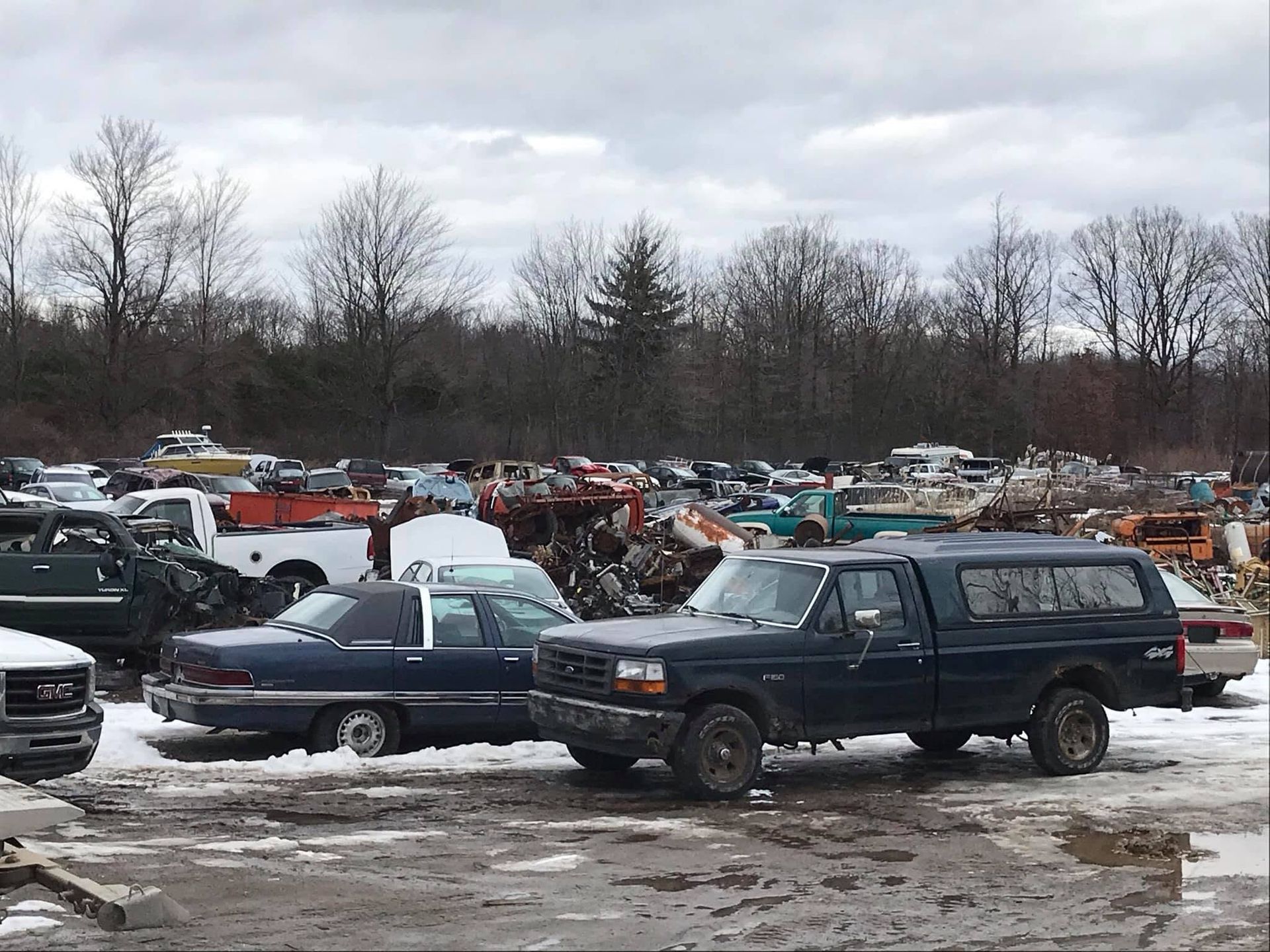 Mechanic wearing gloves pulls wiring from a damaged car trunk in a scrapyard.