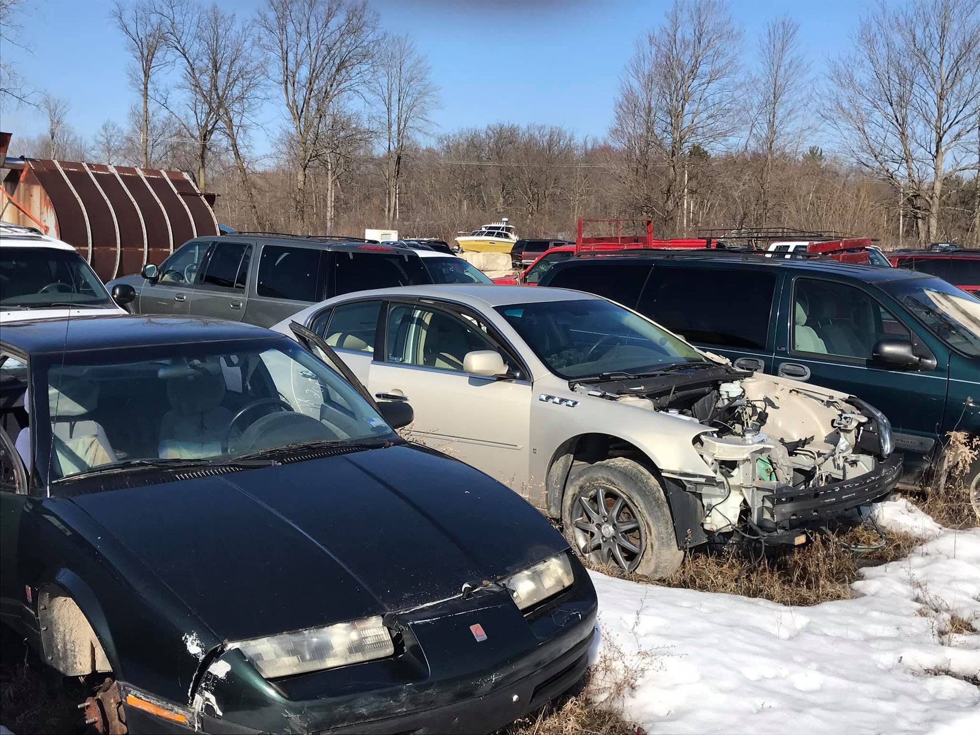 Damaged cars parked in a snowy lot, including a black car and a white car with a missing front end