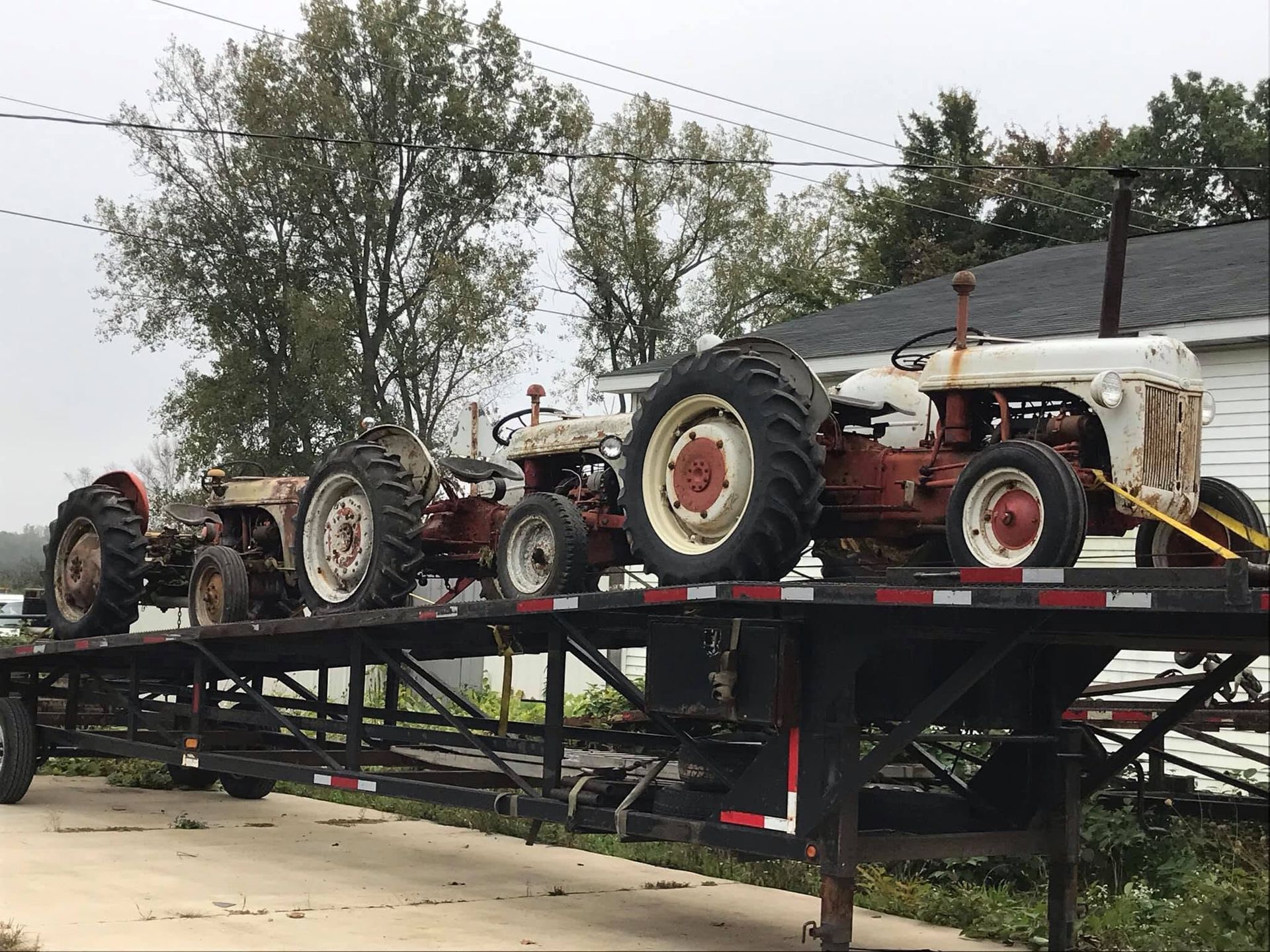 Old tractors loaded on a black trailer at an outdoor farm equipment display