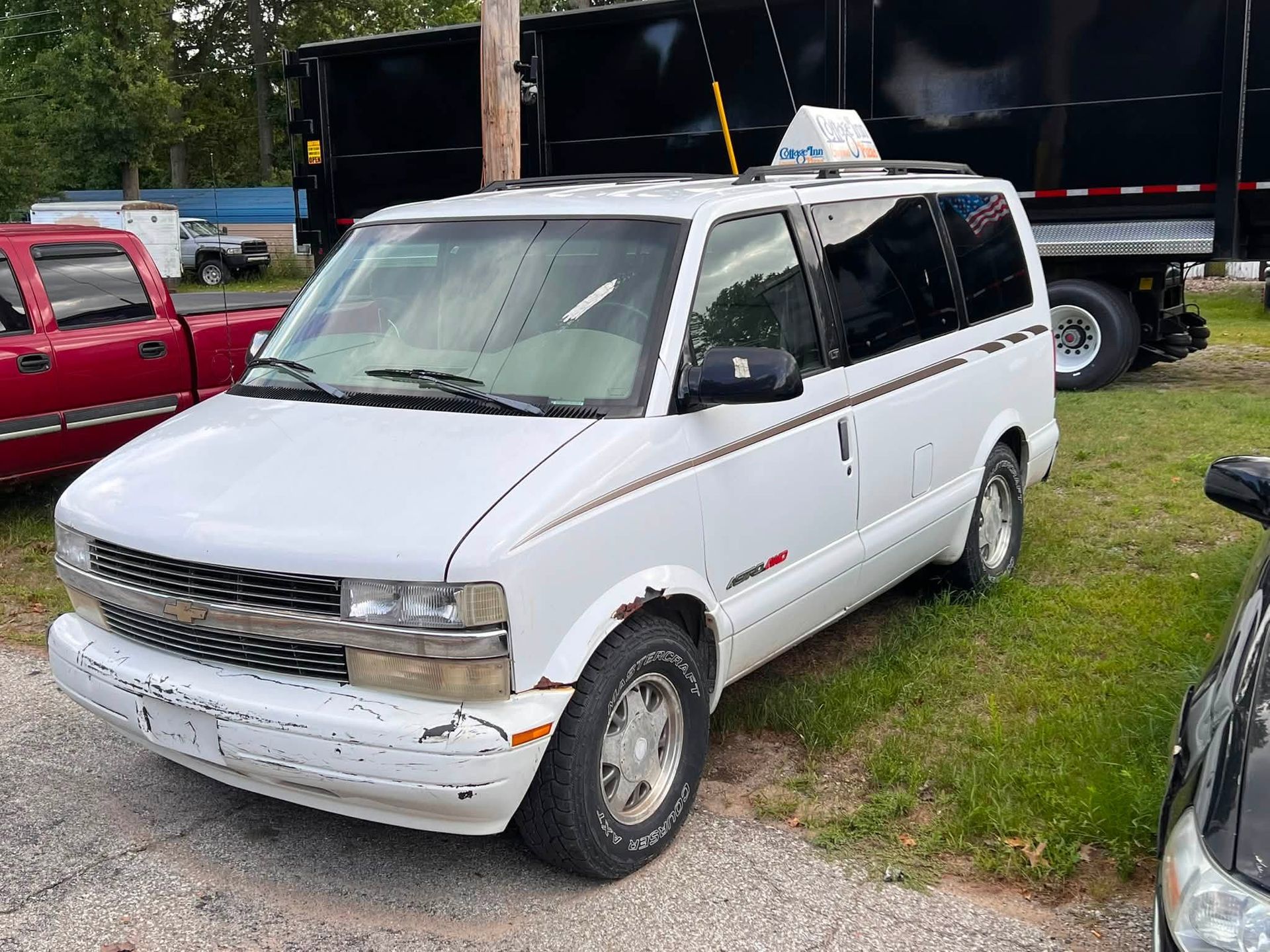 White cargo van parked on grass beside a red pickup and a black trailer.