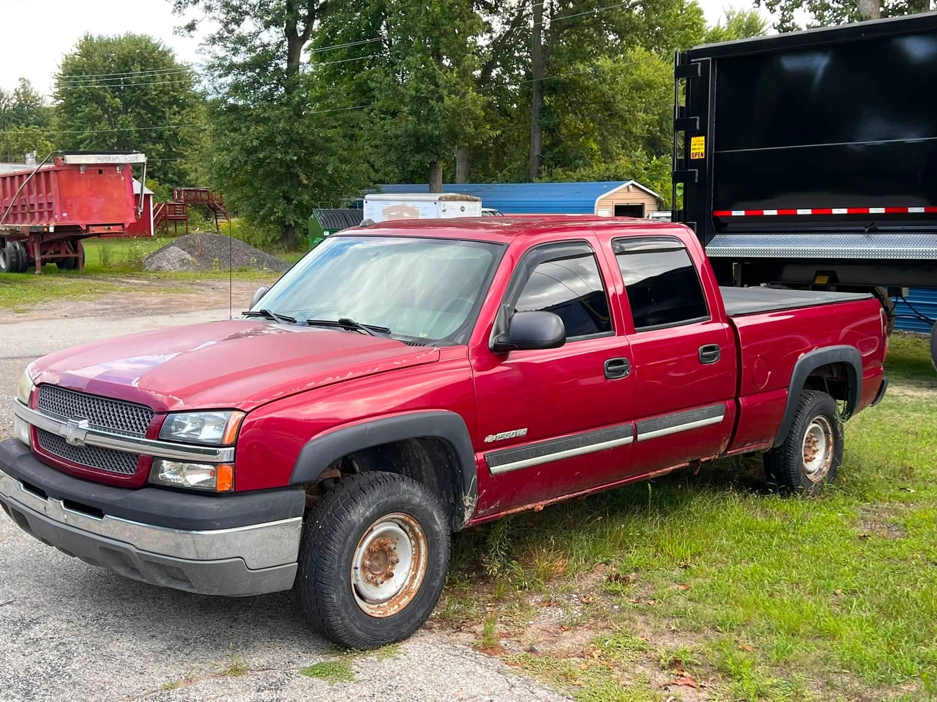 Red pickup truck parked on grass beside a black trailer in a rural area