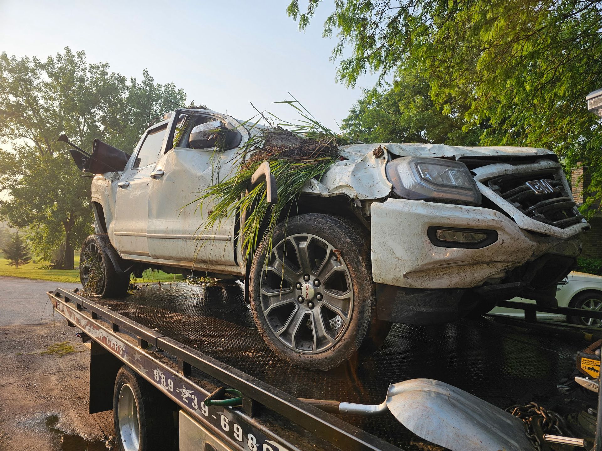 Red tow truck lifting a beige car by its front wheel on a cobblestone street