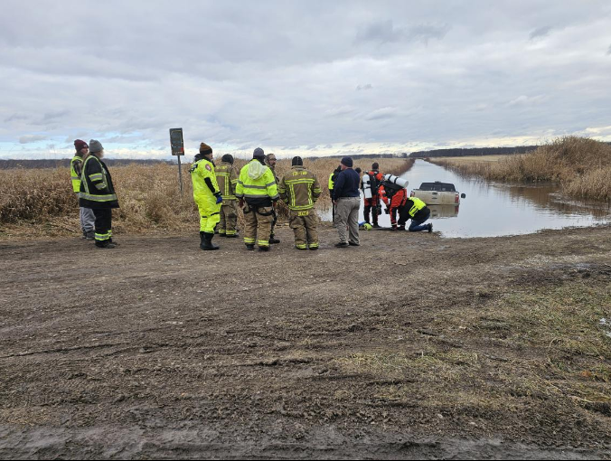 Emergency responders in neon jackets gather at a muddy roadside beside a flooded ditch