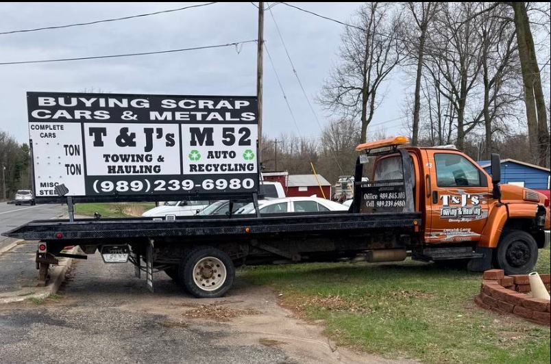 Orange tow truck parked beside a scrap yard sign advertising buying scrap cars and metals