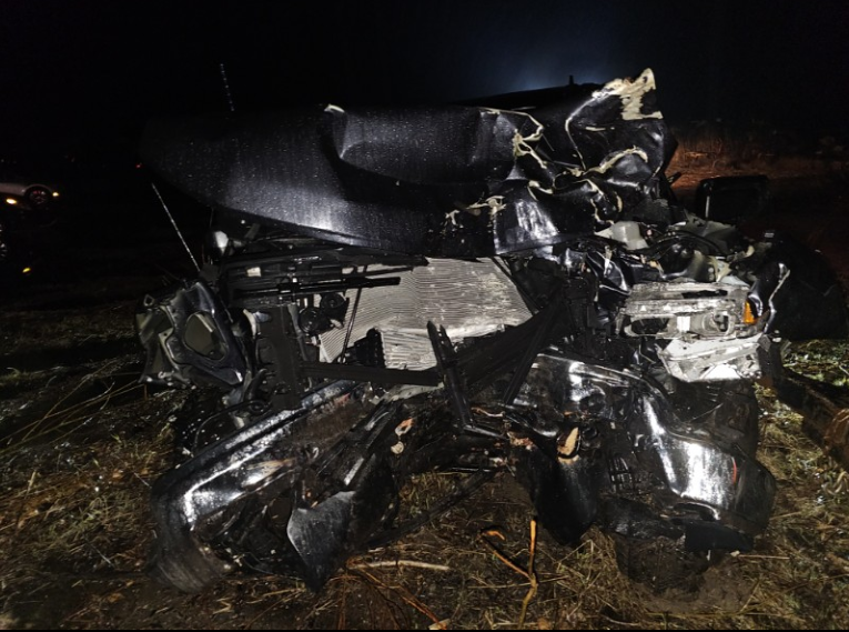 Severely mangled black car wreckage at night on a dark roadside
