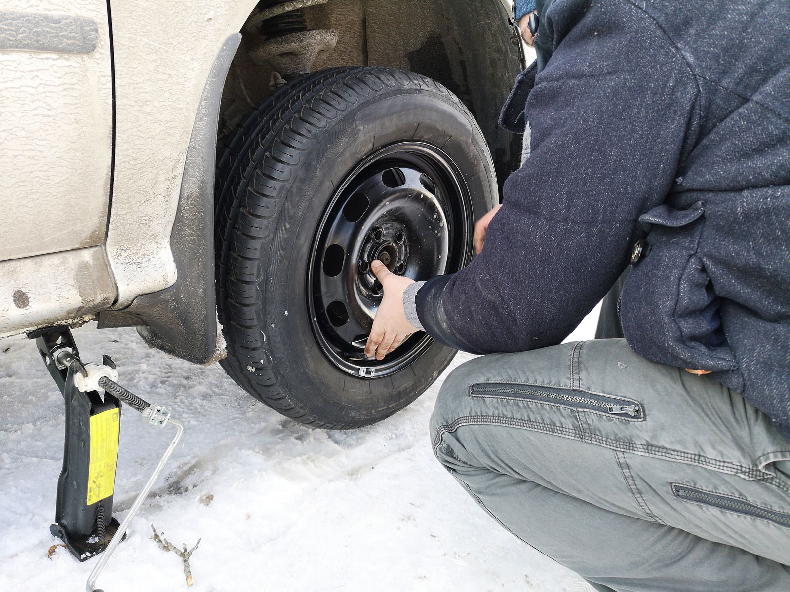 Person changing a tire on a vehicle in the snow using a jack.