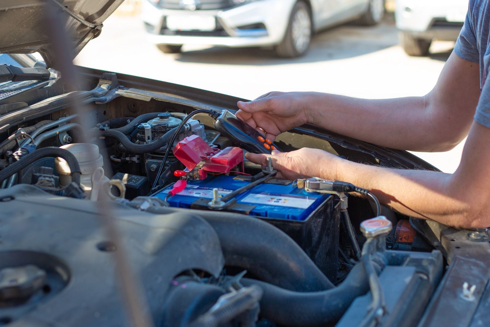 Mechanic working on a car engine with a blue battery and red jumper cables