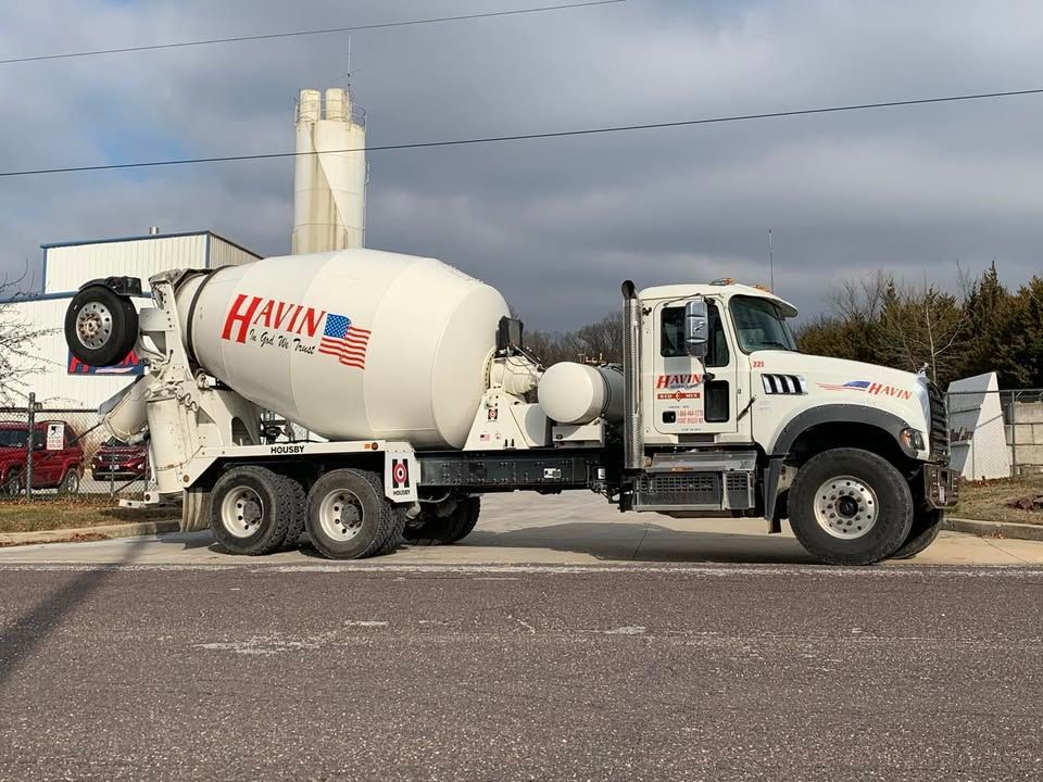 White cement mixer truck parked on a roadside under cloudy sky