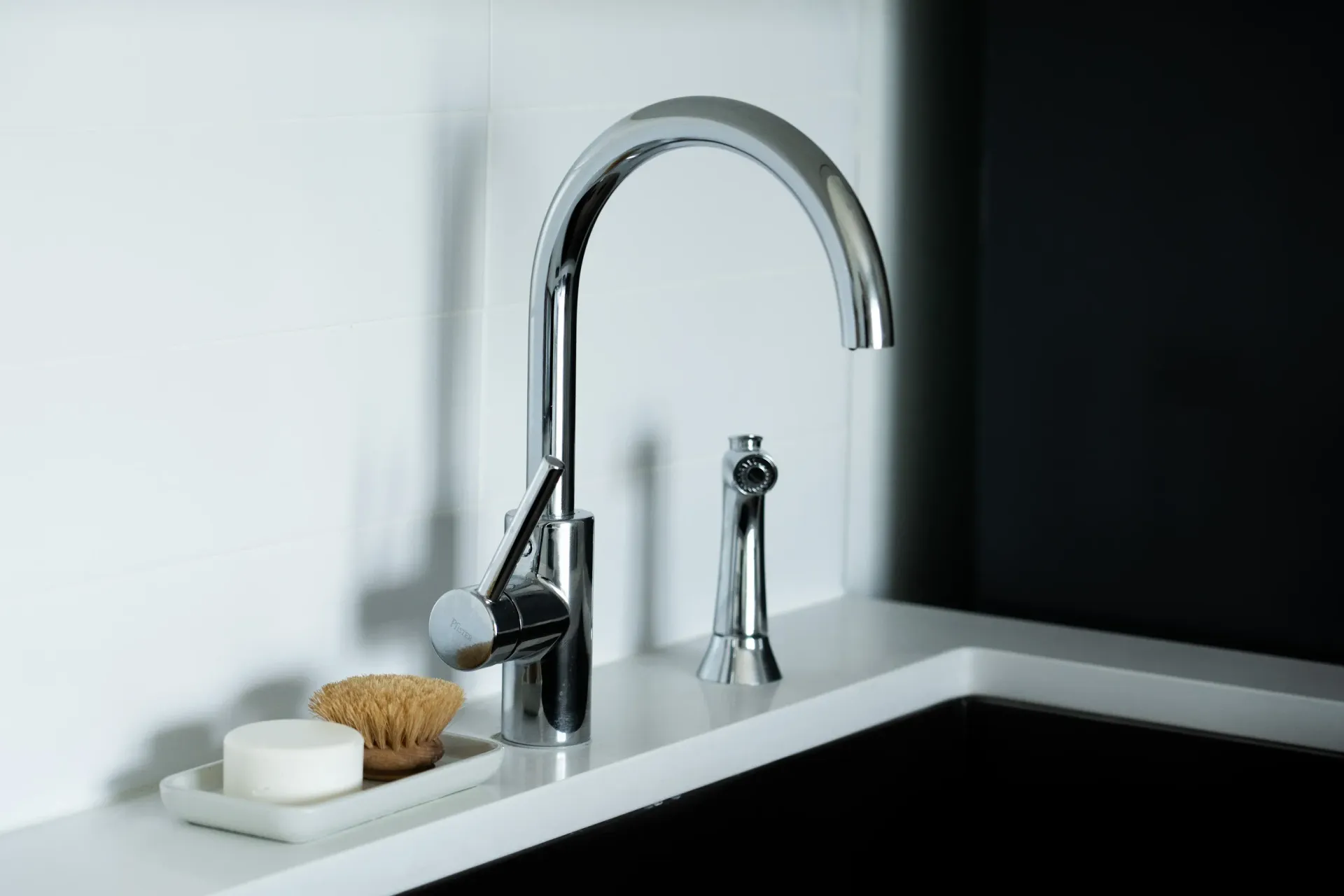 Chrome kitchen faucet with sprayer against white and black surfaces.