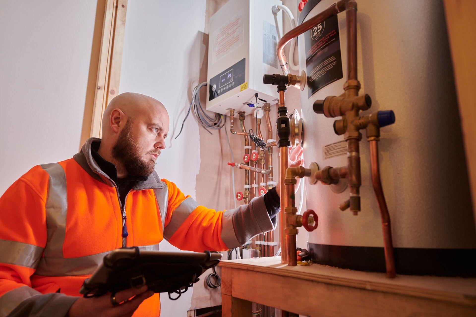 A man is working on a water heater while holding a tablet.