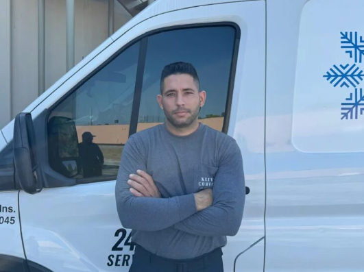 Man with crossed arms in front of a white van with a logo of snowflakes. 24-hour service written on the van.