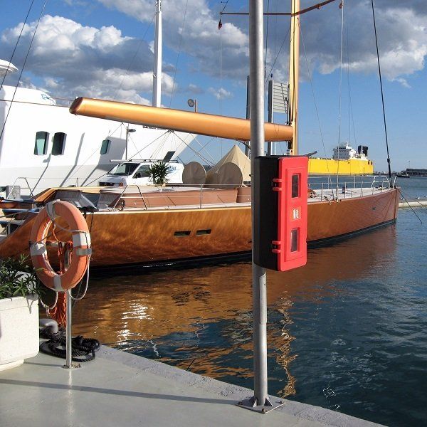 Een houten zeilboot ligt aangemeerd in een haven, met op de voorgrond een rode kluis op een paal.