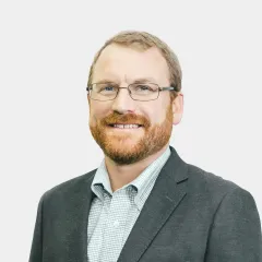 A man with a beard and glasses is wearing a suit and smiling.