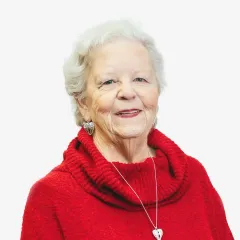 An elderly woman wearing a red sweater and a heart necklace