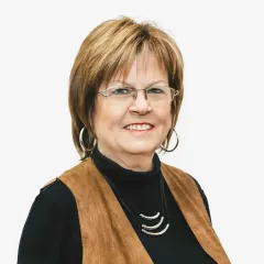 A woman wearing glasses and a brown vest is smiling for the camera.