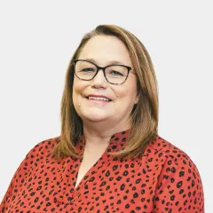 A woman wearing glasses and a leopard print shirt is smiling.