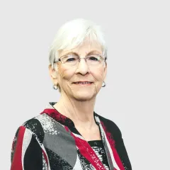 An older woman wearing glasses and a plaid shirt is smiling for the camera.