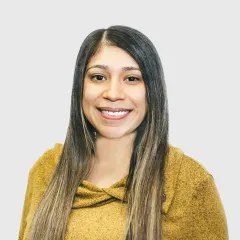 A woman with long hair is wearing a yellow sweater and smiling.