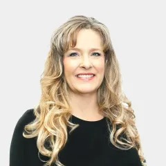 A woman with long blonde hair is wearing a black shirt and smiling.
