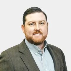 A man with a beard is wearing a suit and smiling for the camera.
