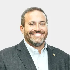 A man with a beard is wearing a suit and smiling.
