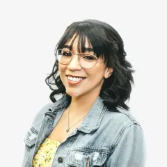 A woman wearing glasses and a denim jacket is smiling.