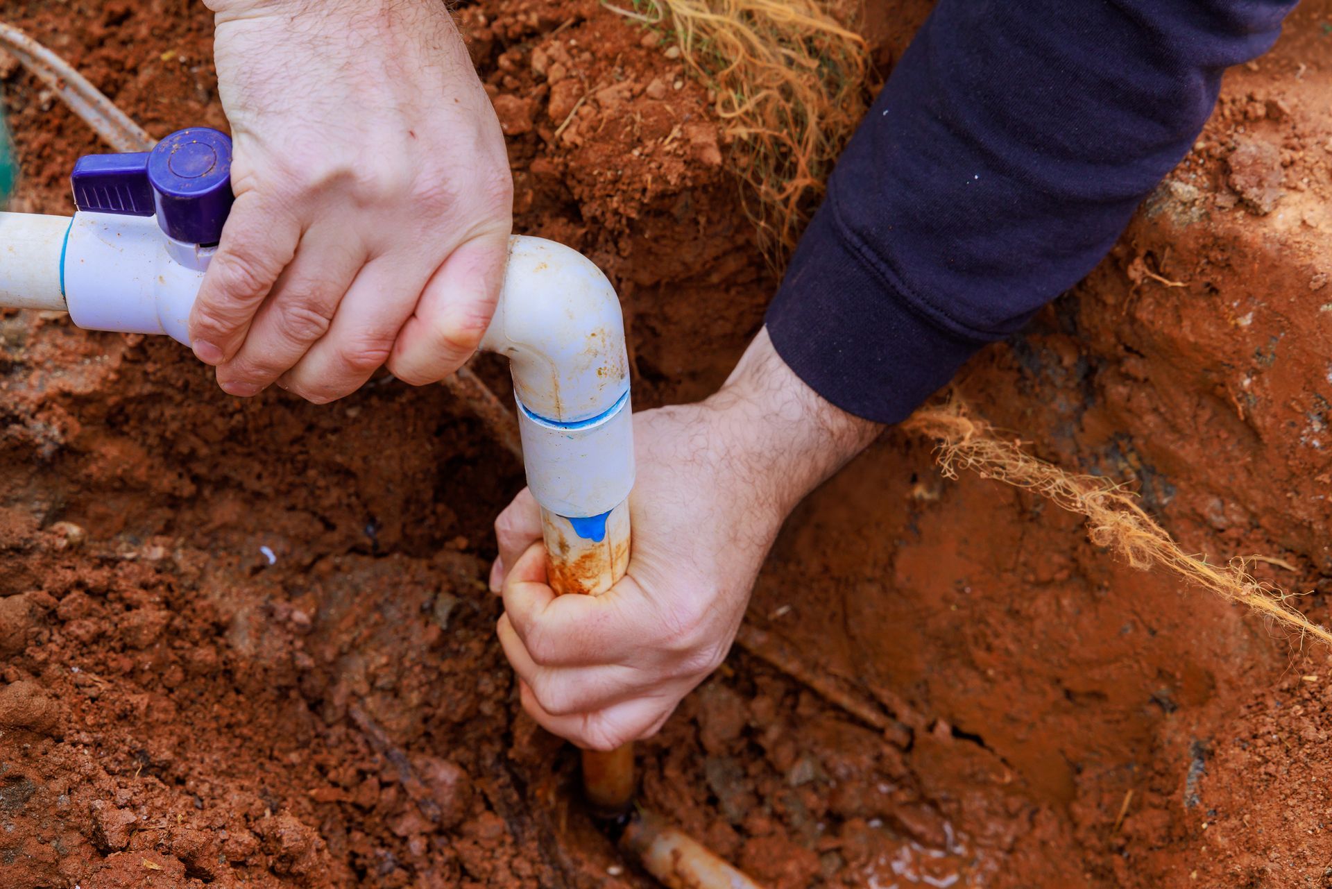 A man is fixing a pipe in the dirt.