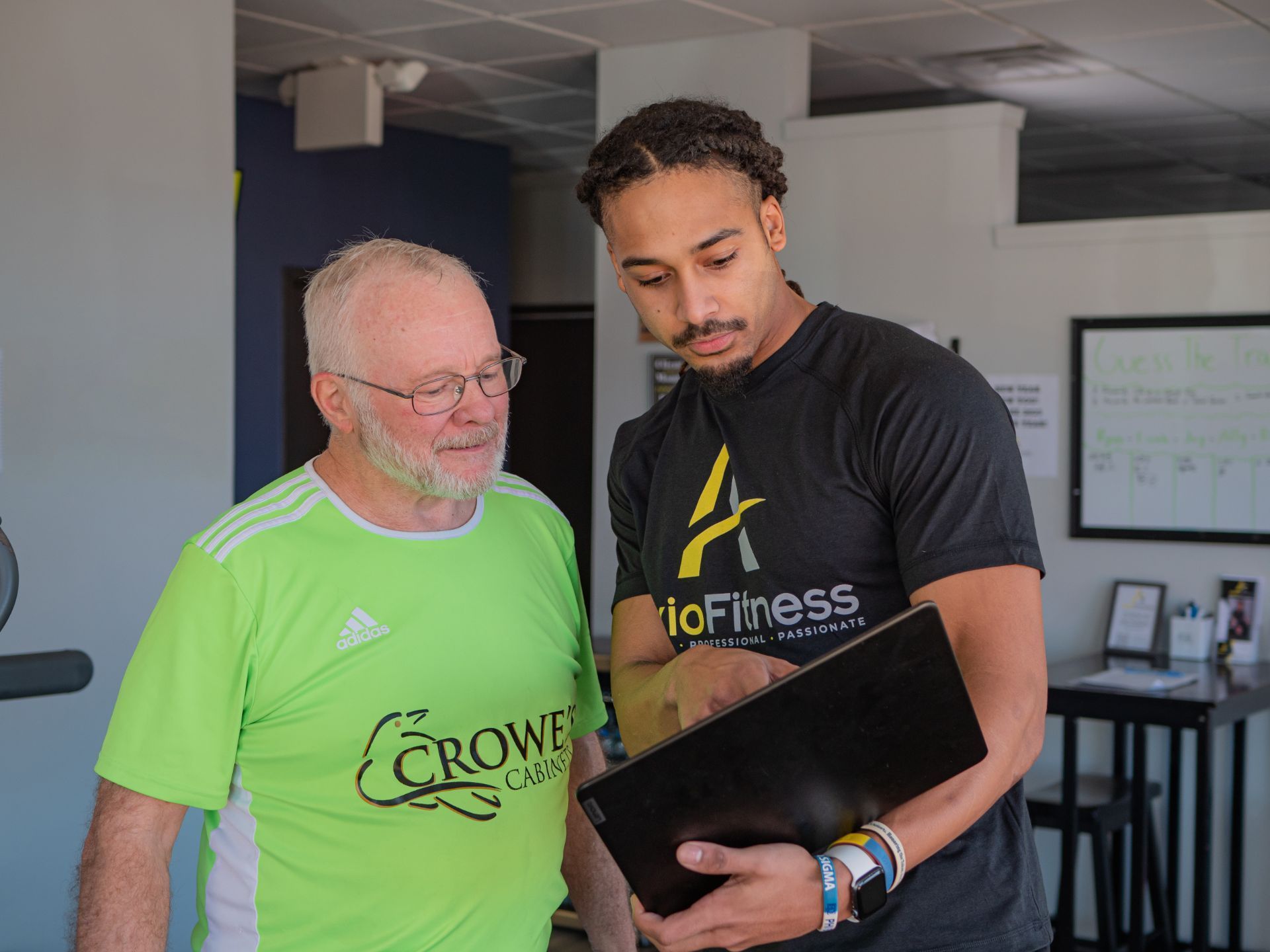 A personal trainer and an older man looking at a document. The trainer wears a black shirt, the man a green shirt.