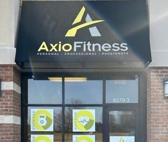Axio Fitness storefront with black awning, yellow and gray logo, and glass doors displaying exercise-themed images.