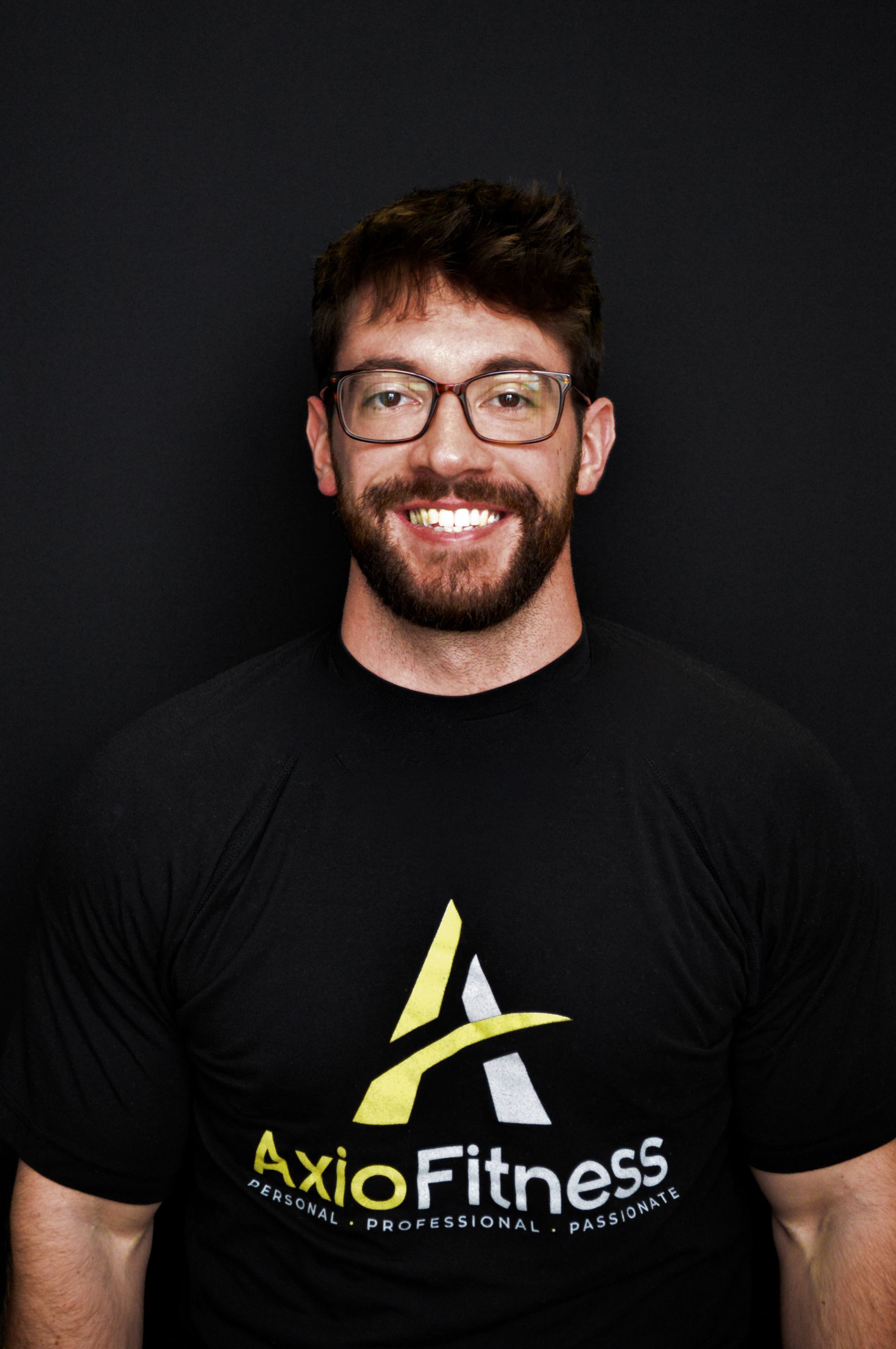 A man with glasses and a beard, wearing a black AxioFitness t-shirt, smiles.